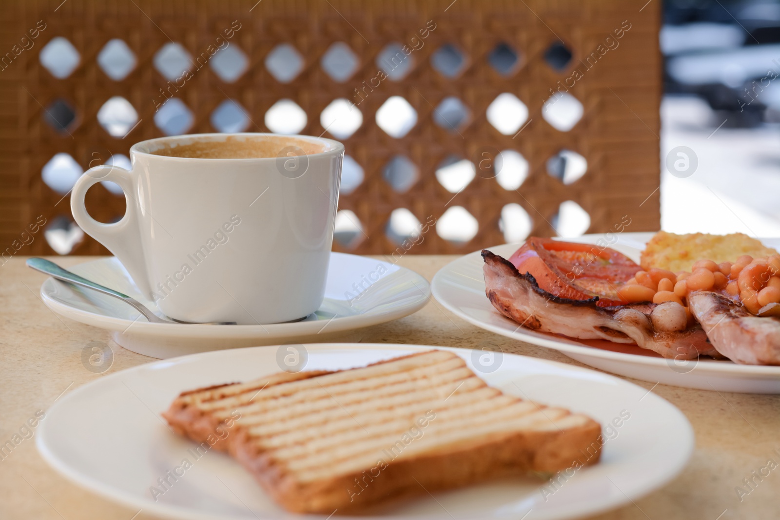 Photo of Delicious breakfast with fried meat and vegetables served on beige table in cafe, closeup