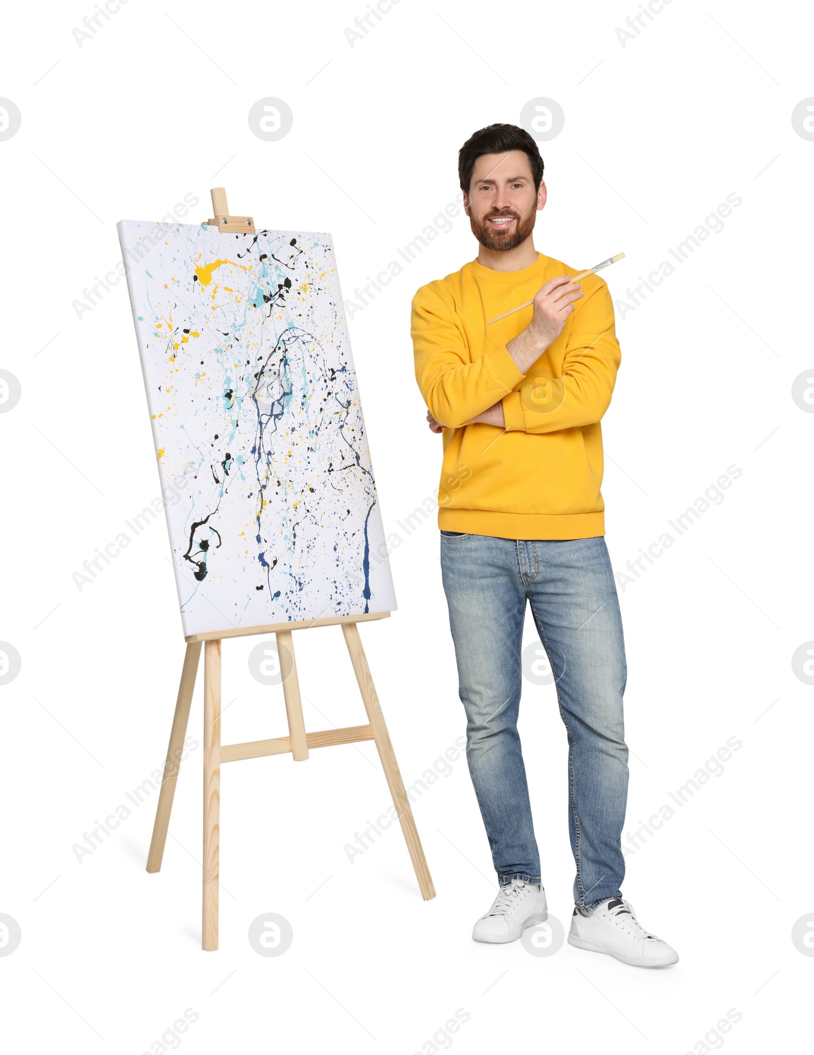 Photo of Happy man with brush near easel with painting on white background. Creative hobby