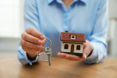 Real estate agent holding house model and key at wooden table, closeup