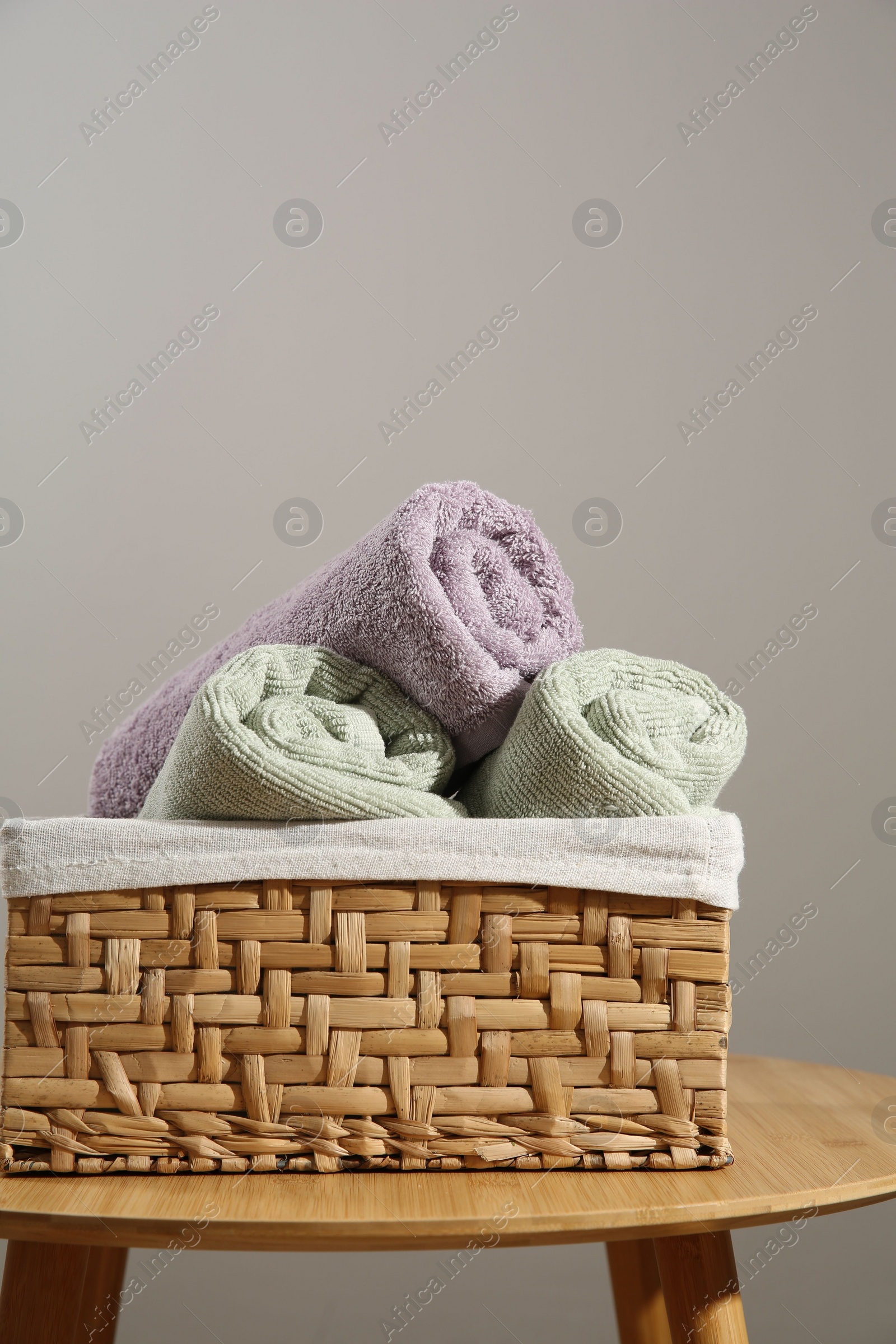 Photo of Clean towels in laundry basket on wooden table against gray background, space for text