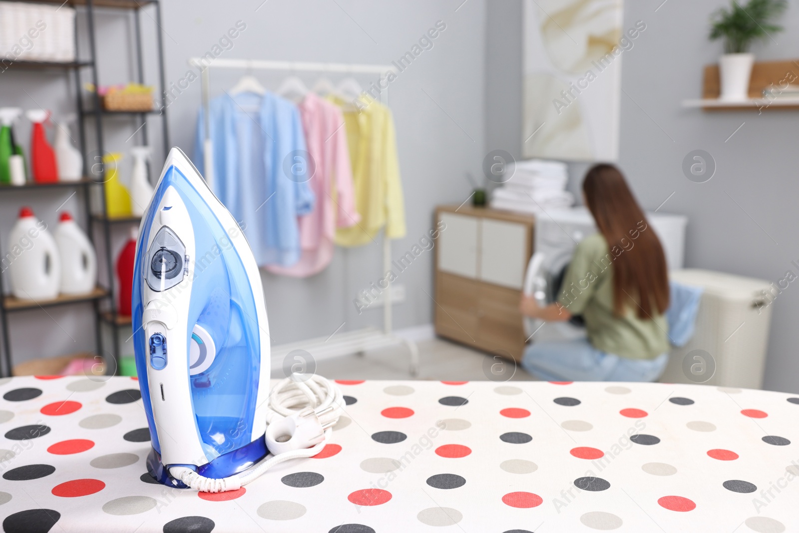 Photo of Woman near washing machine, focus on clothes iron in laundry room