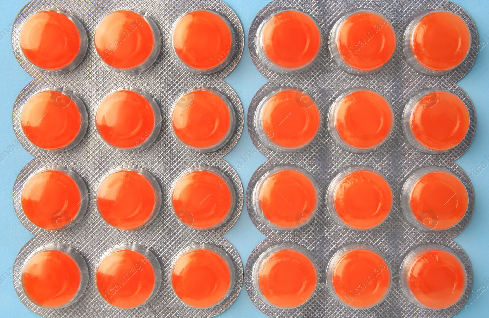 Photo of Blisters with orange cough drops on light blue background, flat lay