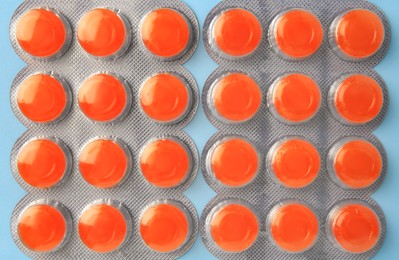 Photo of Blisters with orange cough drops on light blue background, flat lay