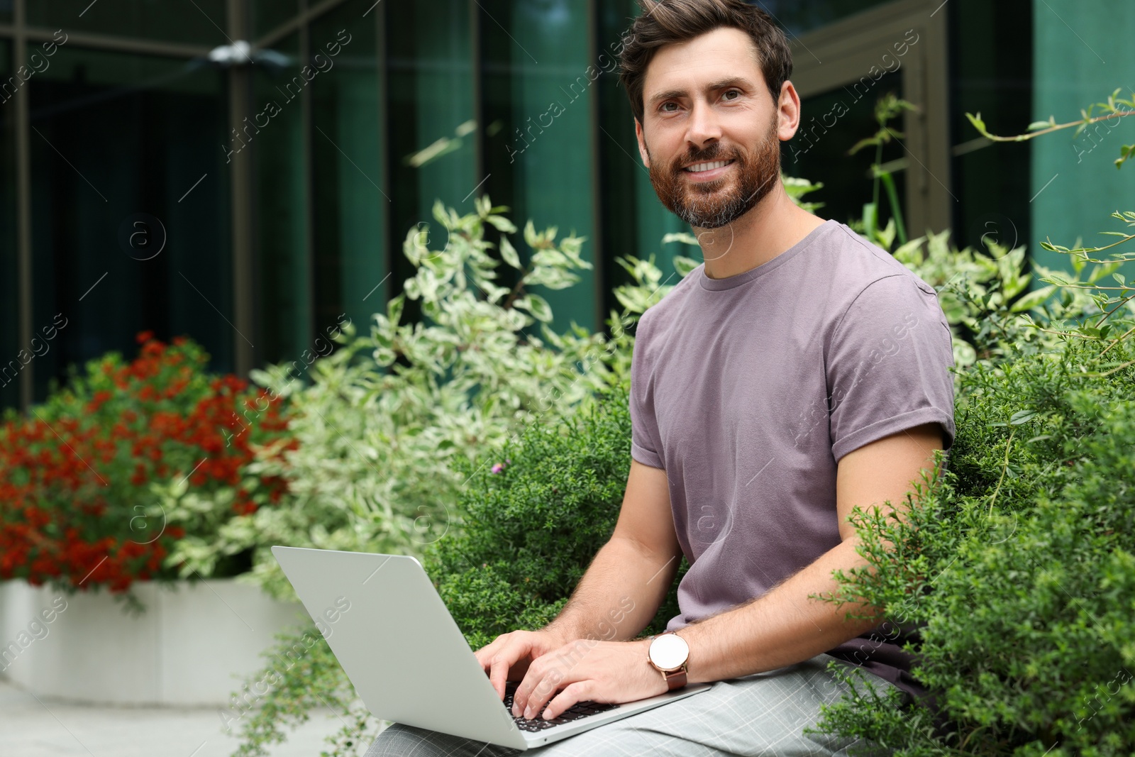 Photo of Handsome man with laptop near beautiful plants on city street