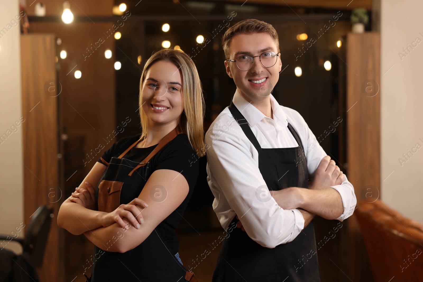 Photo of Portrait of professional hairdressers wearing aprons in beauty salon