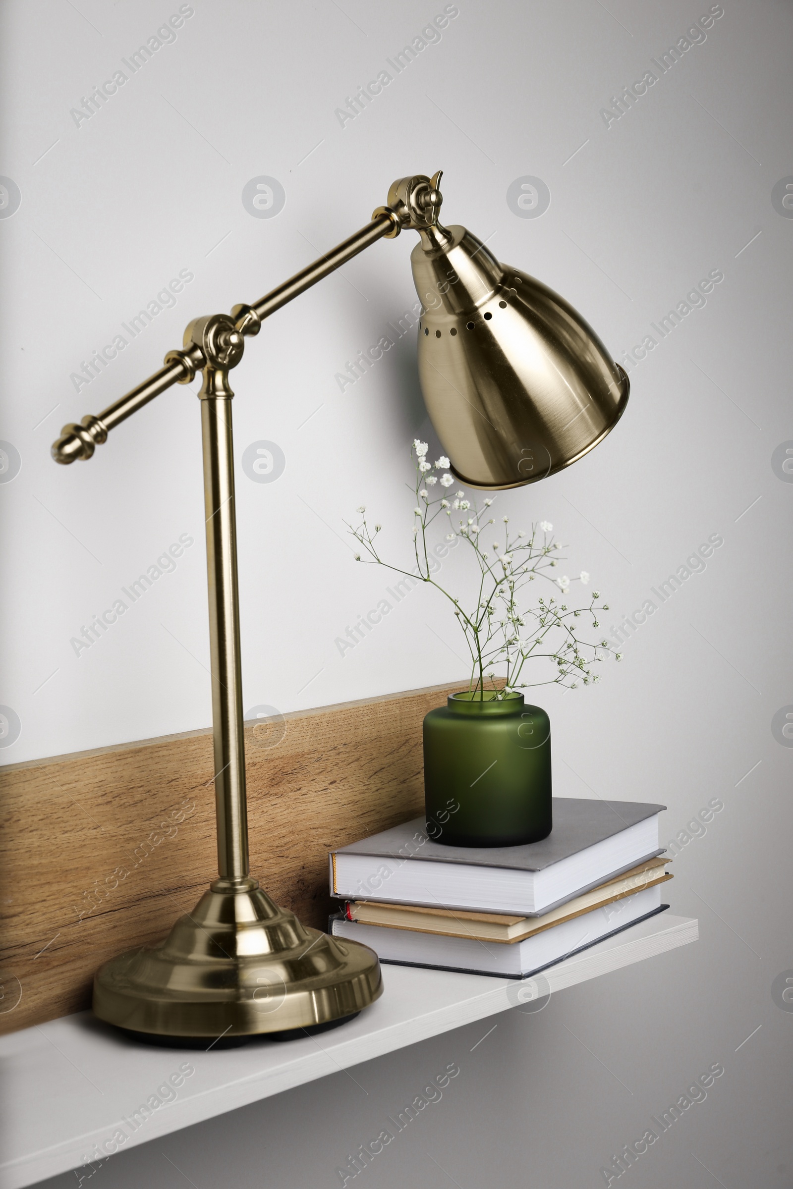Photo of Lamp, vase with gypsophila flowers and stack of books on shelf indoors