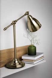 Lamp, vase with gypsophila flowers and stack of books on shelf indoors
