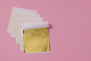 Photo of Edible gold leaf sheets on pink background, top view. Space for text
