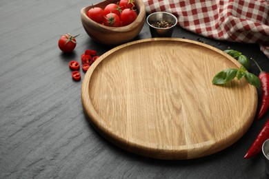 Photo of Cutting board, spices, basil, tomatoes and chili peppers on black textured table. Space for text