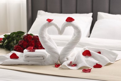 Photo of Honeymoon. Swans made of towels and beautiful red roses on bed in room