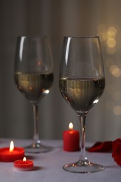 Photo of Glasses of white wine and burning candles on grey table against blurred lights. Romantic atmosphere