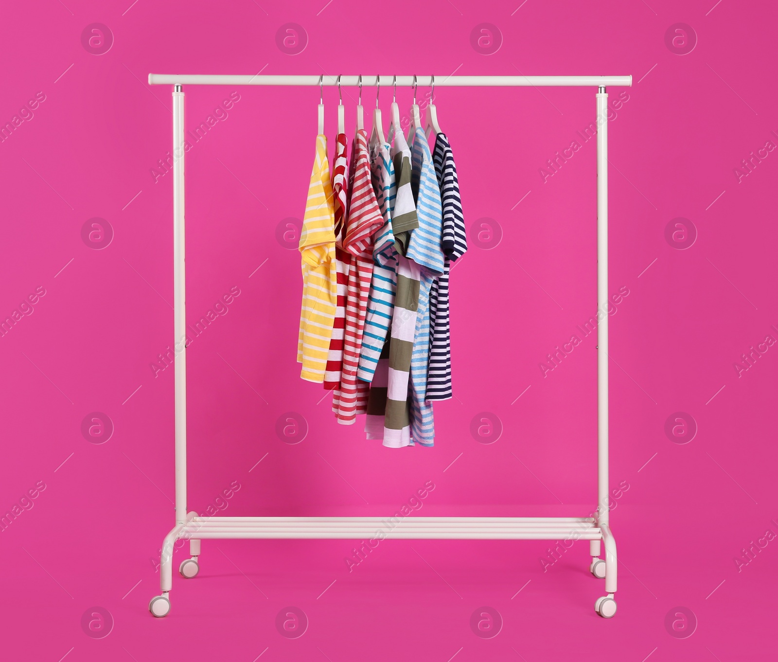 Photo of Colorful clothes hanging on rack against pink background