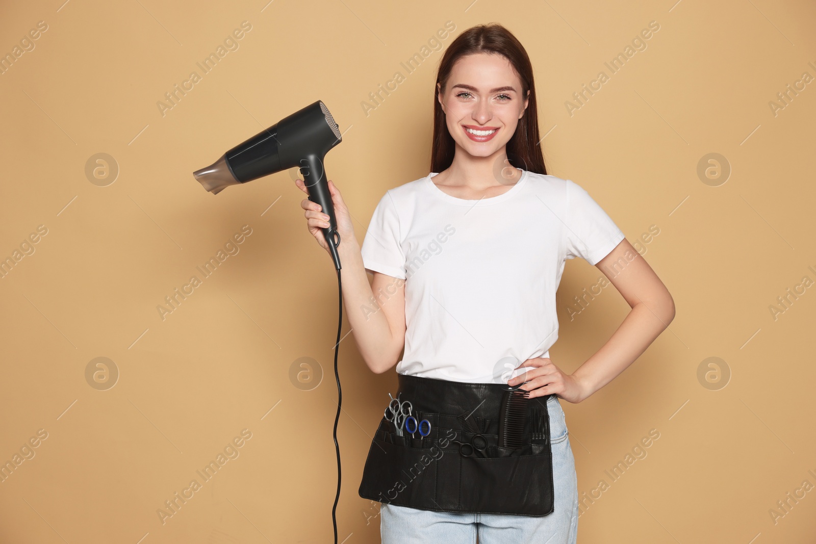 Photo of Portrait of happy hairdresser with hairdryer on beige background