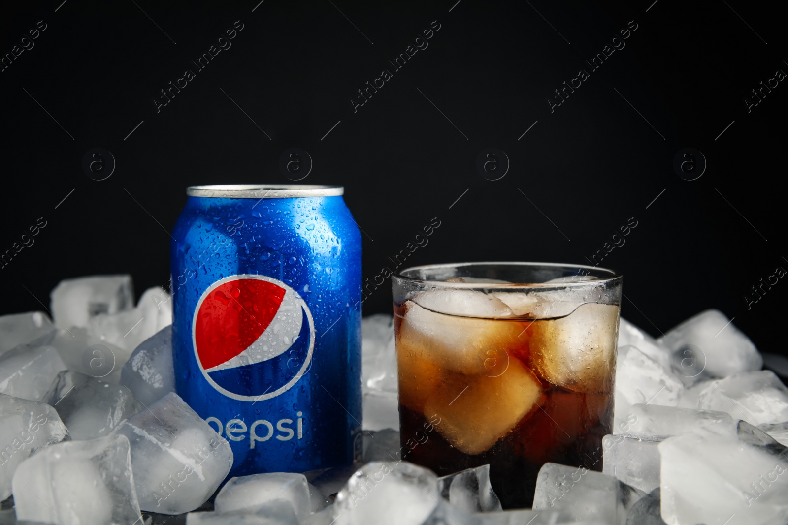 Photo of MYKOLAIV, UKRAINE - FEBRUARY 11, 2021: Glass of Pepsi and can on ice cubes against black background