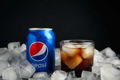 MYKOLAIV, UKRAINE - FEBRUARY 11, 2021: Glass of Pepsi and can on ice cubes against black background