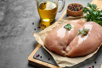 Wooden board with raw chicken breasts, pepper and parsley near olive oil in pitcher on table