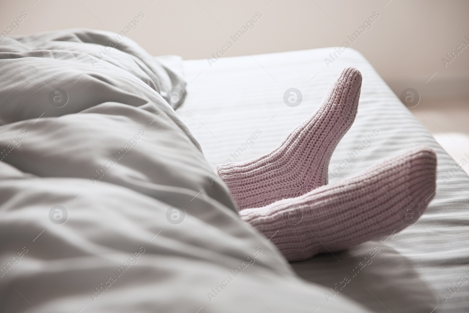 Photo of Woman wearing knitted socks under blanket in bed, closeup