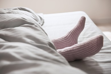 Woman wearing knitted socks under blanket in bed, closeup