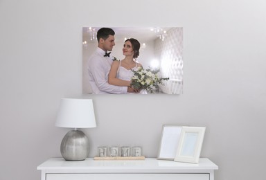 Canvas with printed photo of happy newlywed couple on white wall in room