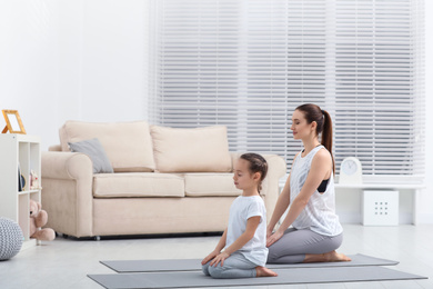 Photo of Young mother with little daughter practicing yoga at home