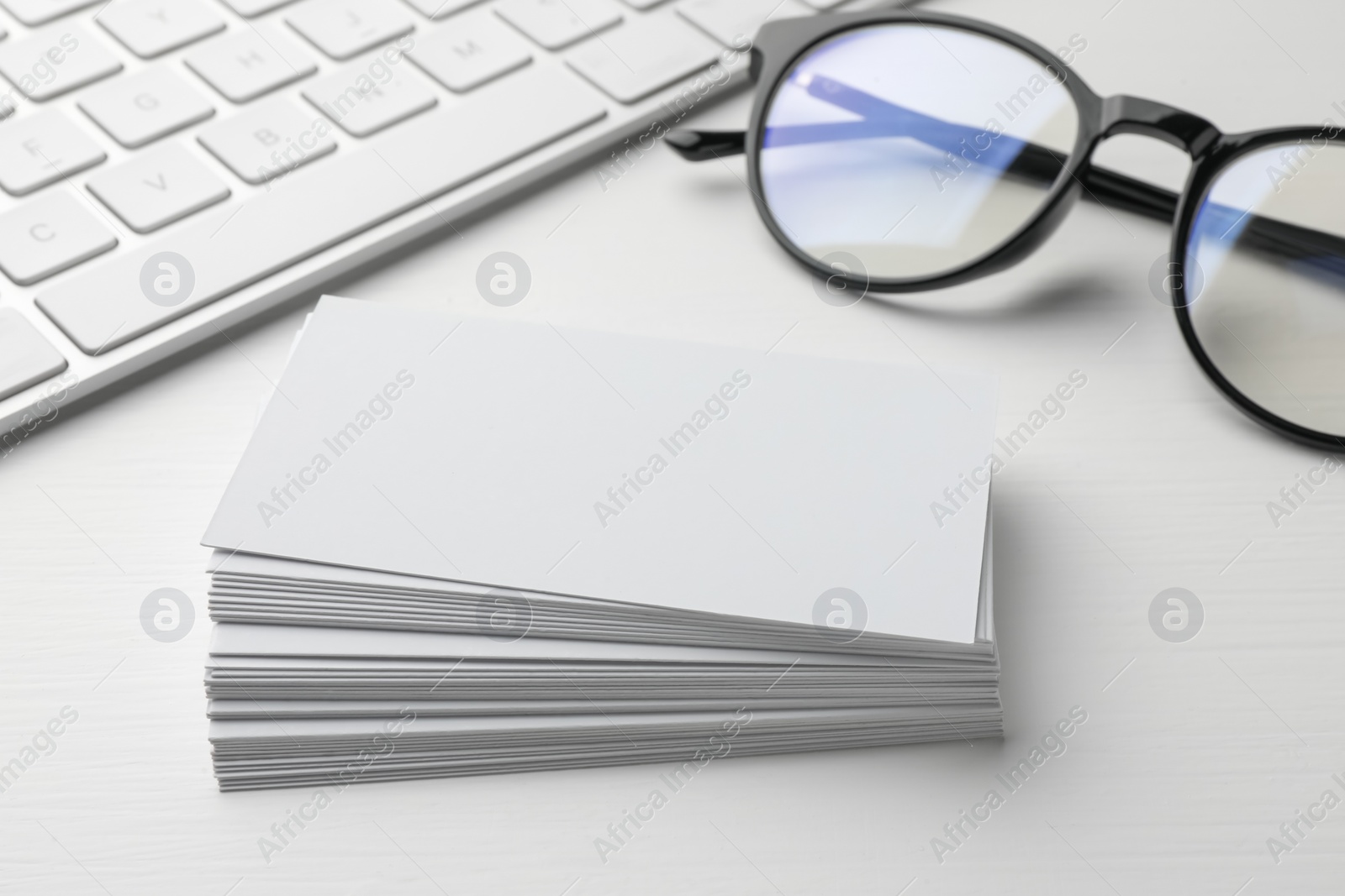 Photo of Blank business cards, glasses and keyboard on white table, closeup. Mockup for design