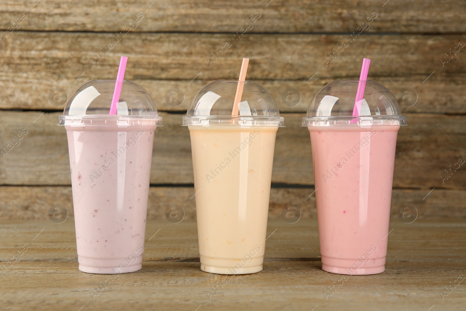 Photo of Plastic cups with different tasty smoothies on wooden table