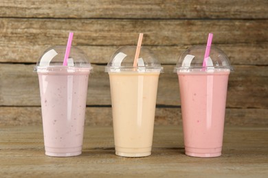 Photo of Plastic cups with different tasty smoothies on wooden table