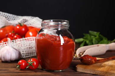 Photo of Jar of tasty tomato paste and ingredients on wooden table