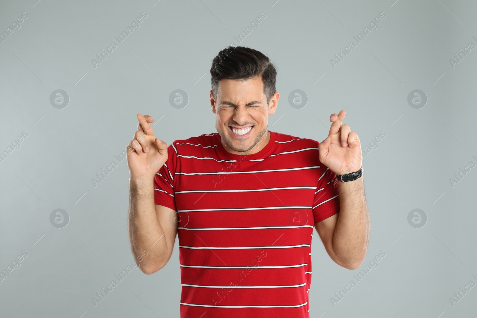 Photo of Man with crossed fingers on grey background. Superstition concept