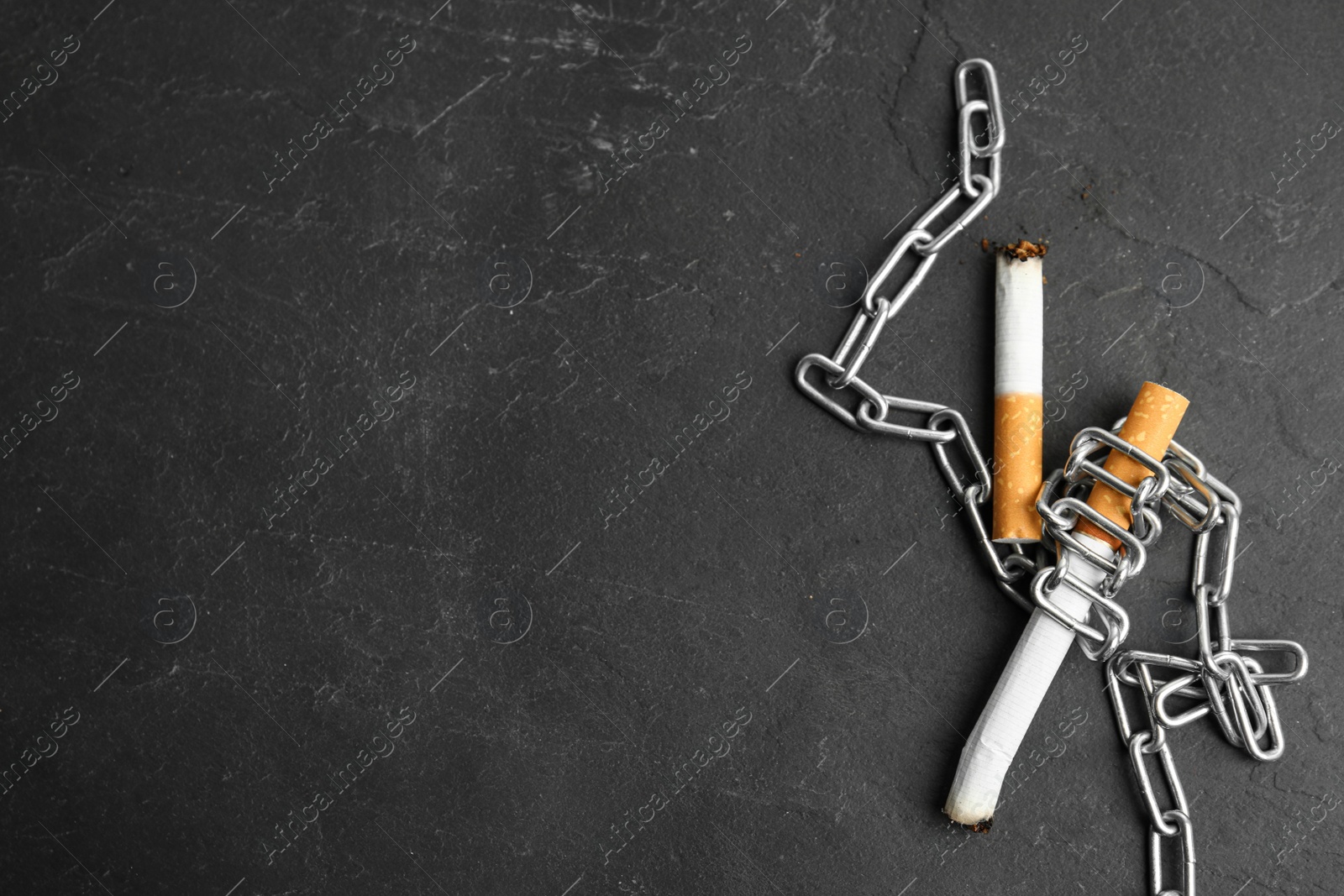 Photo of Cigarette stubs and chain on black table, flat lay with space for text. Quitting smoking concept