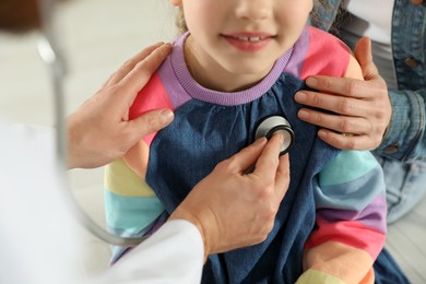 Photo of Mother and daughter having appointment with doctor. Pediatrician examining patient with stethoscope, closeup