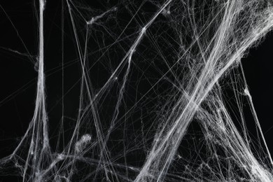 Photo of Creepy white cobweb on black background, closeup