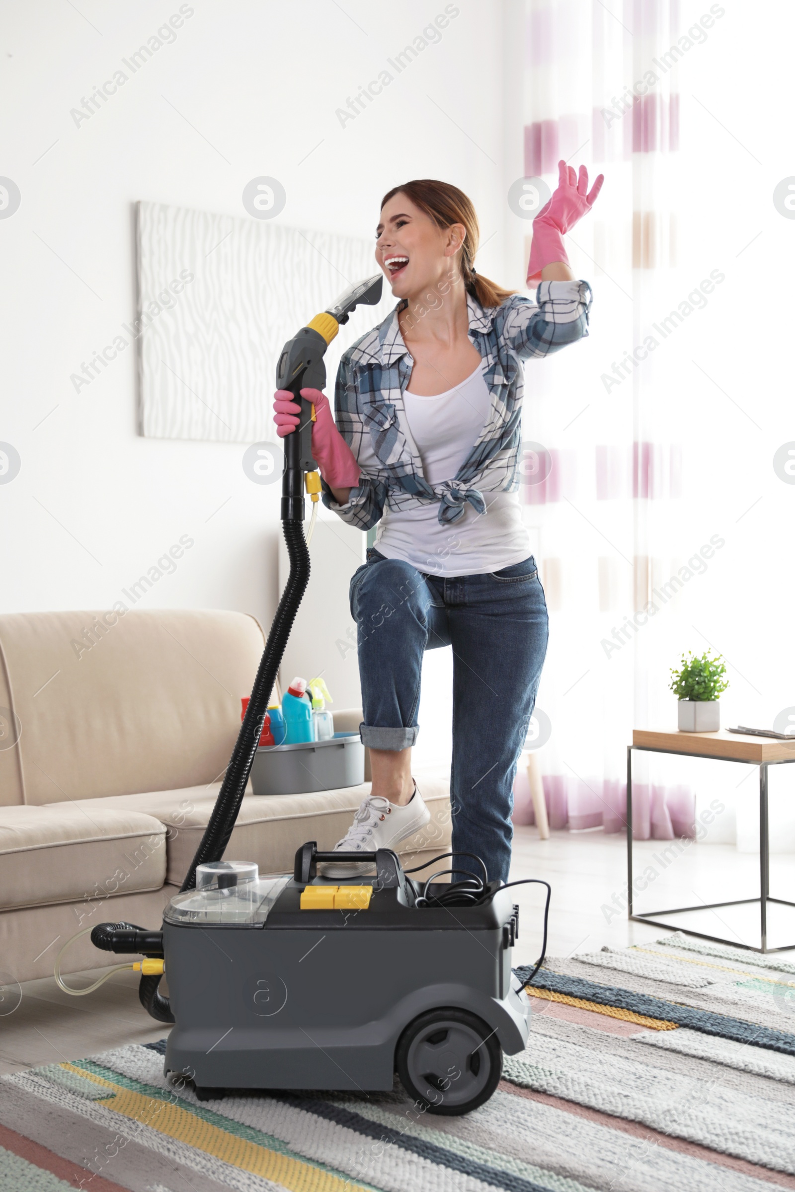 Photo of Happy young woman cleaning home with vacuum cleaner and having fun indoors