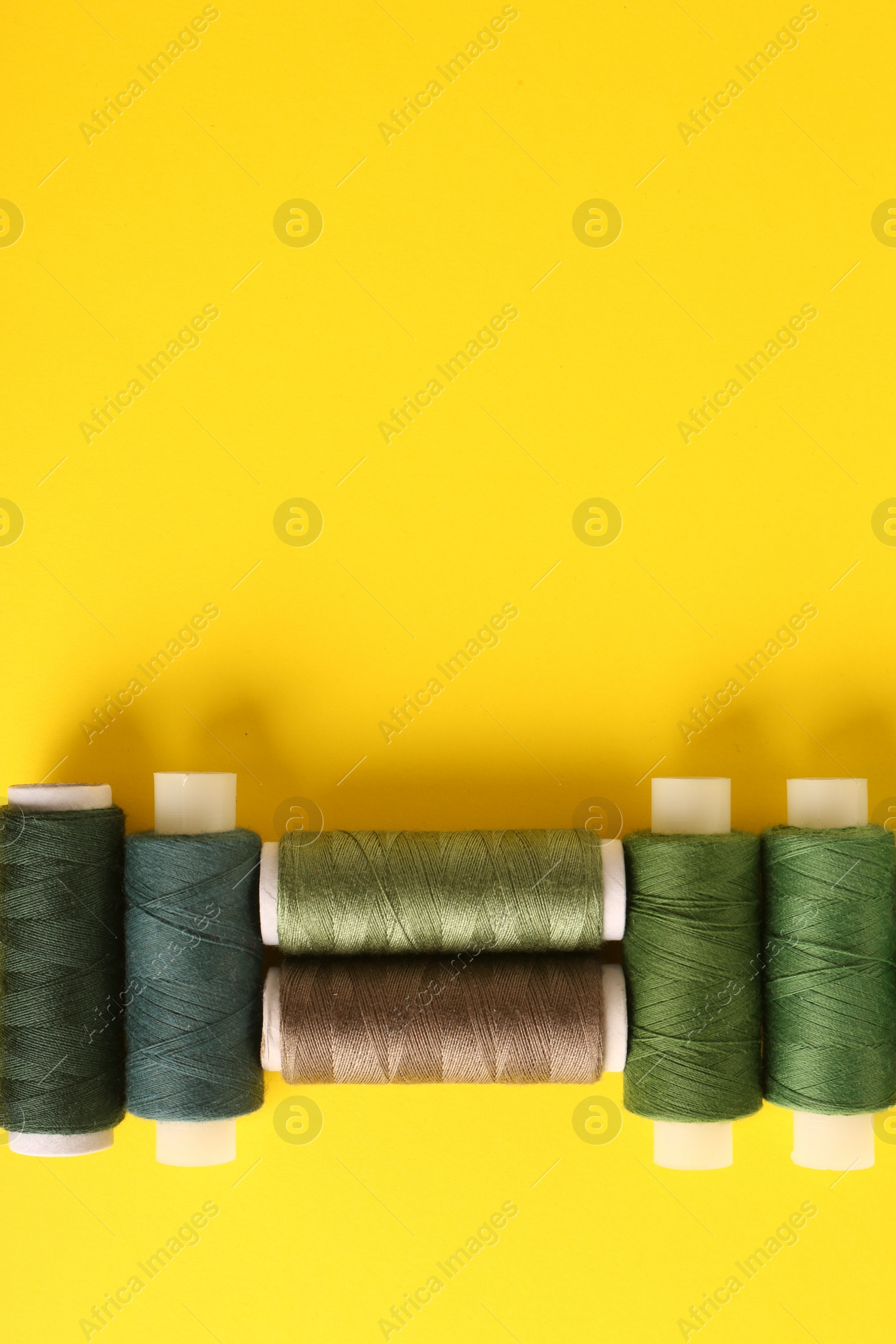 Photo of Different shades of green sewing threads on yellow background, flat lay. Space for text