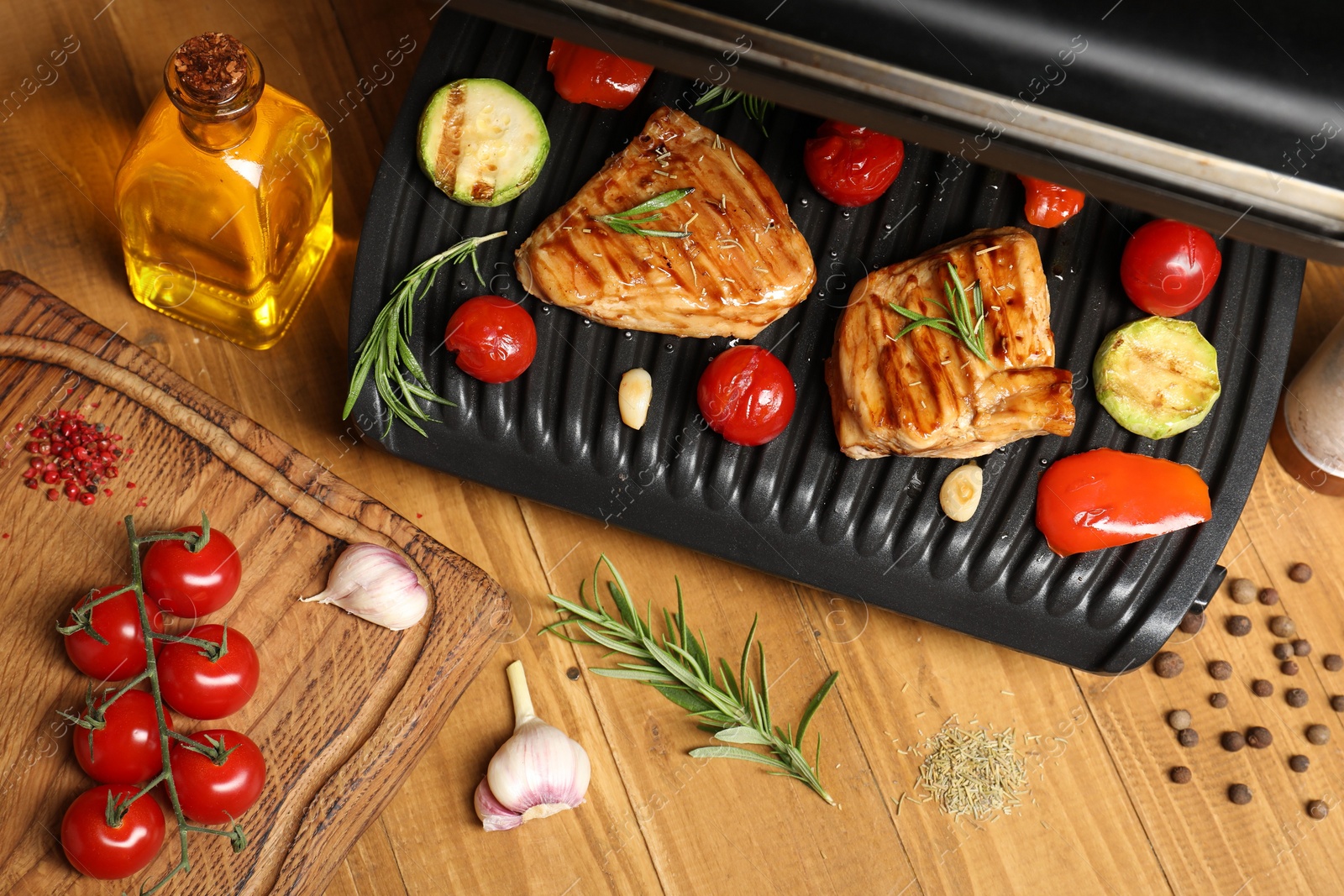 Photo of Electric grill with different products on wooden table, above view