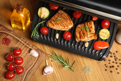 Electric grill with different products on wooden table, above view