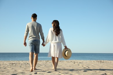 Photo of Young couple walking on beach near sea, back view. Honeymoon trip