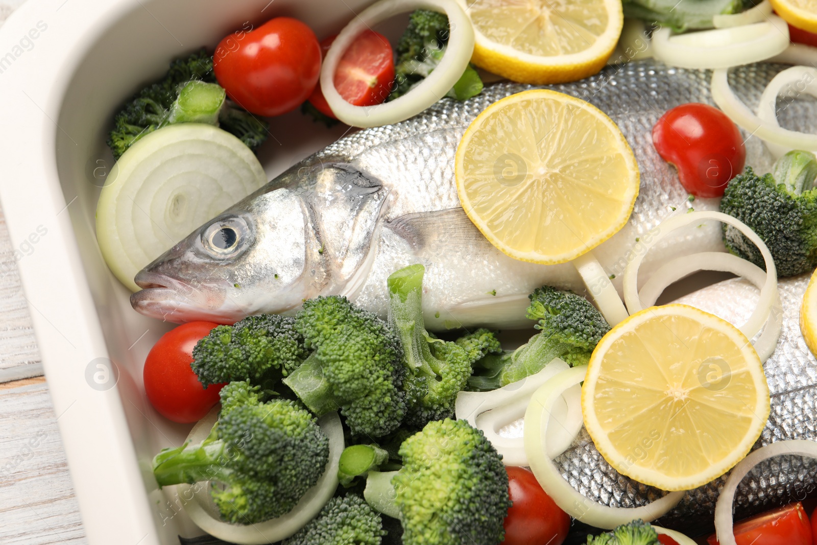 Photo of Raw fish with vegetables and lemon in baking dish on table