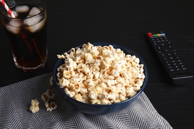 Photo of Bowl with popcorn, glass of iced cola and TV remote on table. Watching cinema