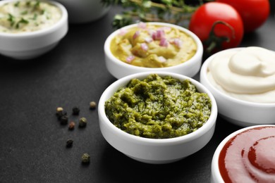 Different tasty sauces in bowls on black table, closeup