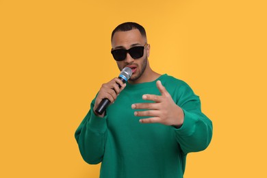 Photo of Handsome man with microphone singing on orange background