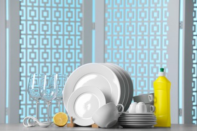 Clean dishware, glasses and bottle of detergent on light grey table