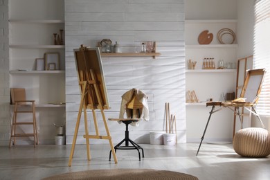 Modern studio interior with wooden easel near large window. Artist's workplace