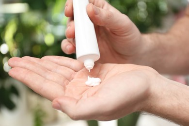 Man applying moisturizing cream from tube onto hand on blurred background, closeup