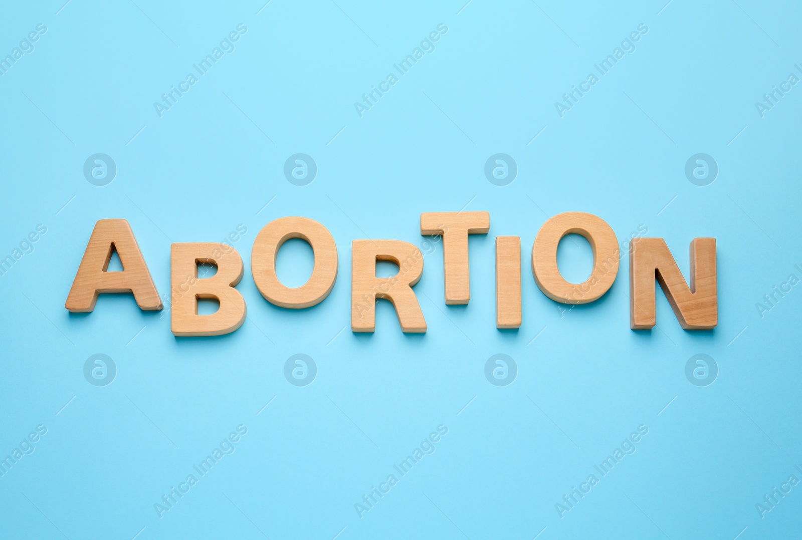 Photo of Word Abortion made of wooden letters on light blue background, flat lay