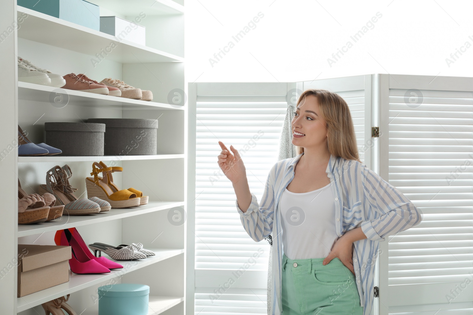 Photo of Woman near rack with shoes indoors. Interior design