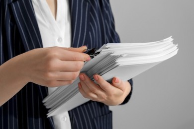 Woman attaching documents with metal binder clip on grey background, closeup