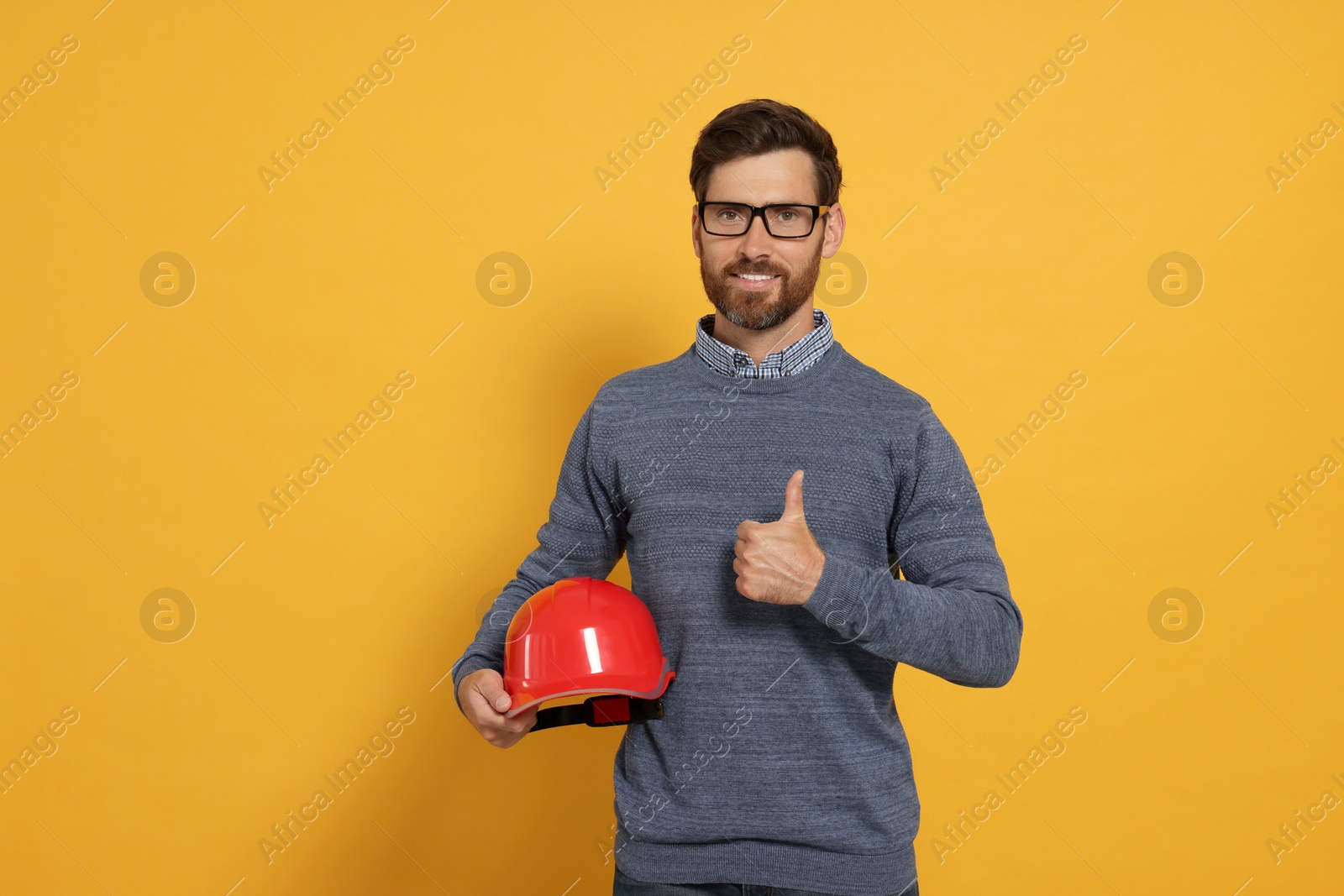 Photo of Professional engineer with hard hat showing thumb up on yellow background
