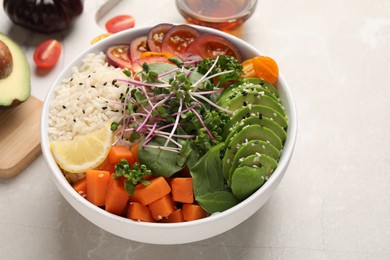 Photo of Delicious vegan bowl with avocados, carrots and microgreens on light grey table, space for text