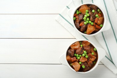 Photo of Delicious beef stew with carrots, peas and potatoes on white wooden table, flat lay. Space for text